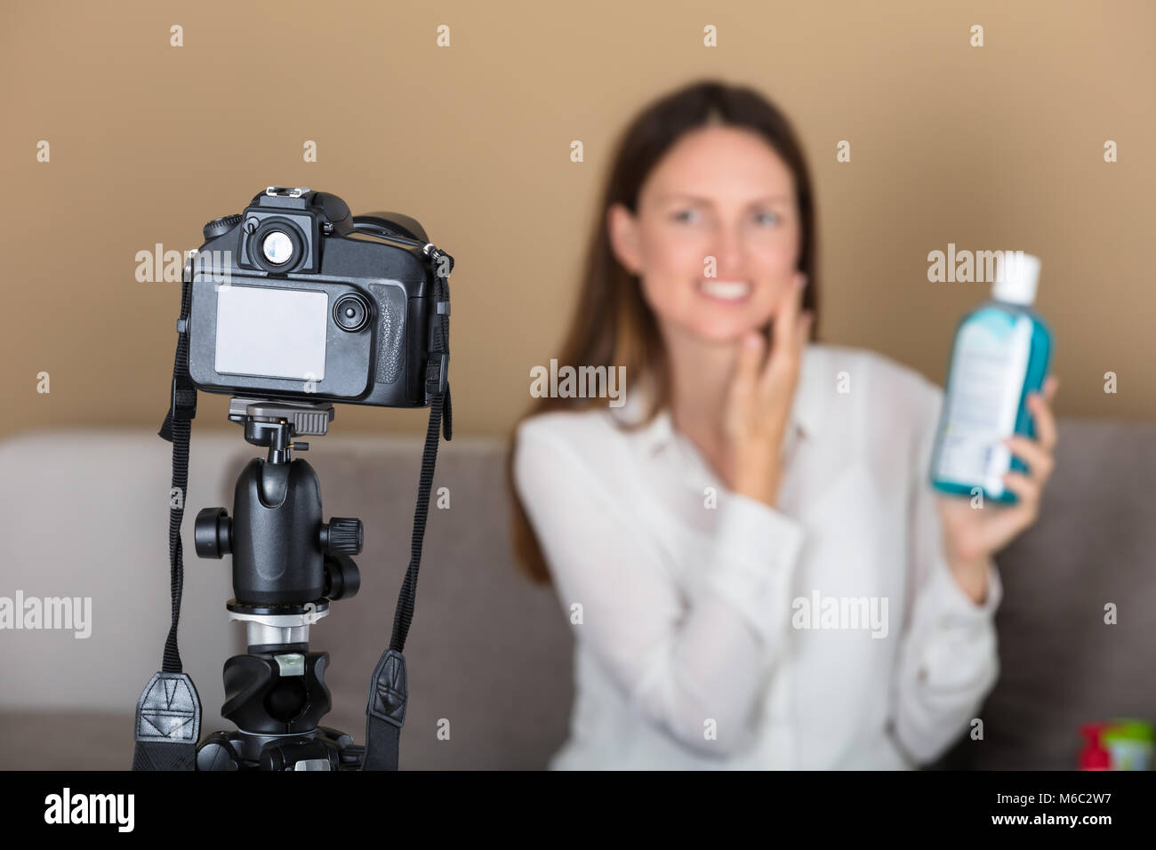 Sorridente femmina giovane blogger tenere il prodotto la registrazione di un video con la fotocamera a casa Foto Stock