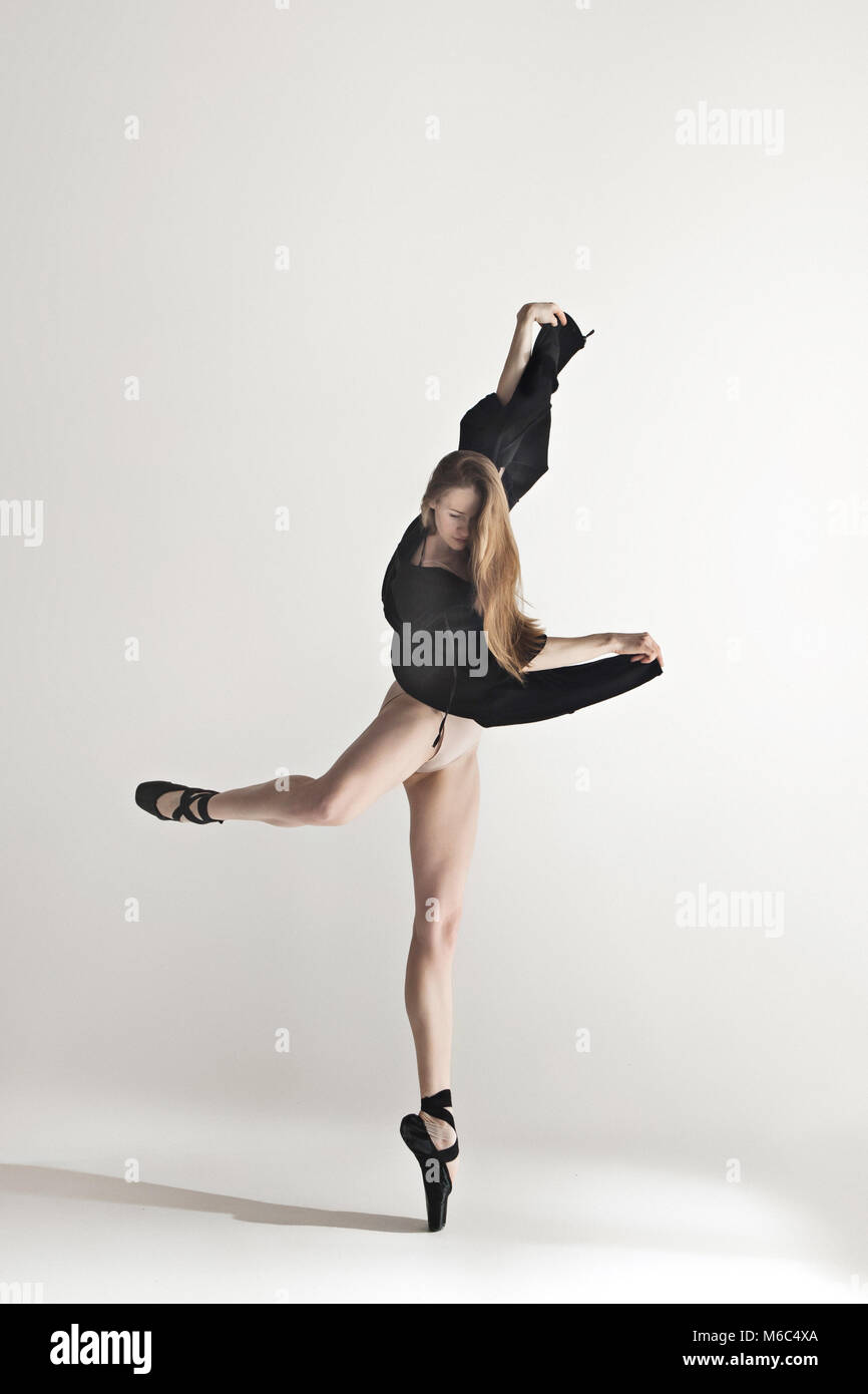 Giovane bellissima ballerina in costume da bagno beige danza su sfondo grigio Foto Stock
