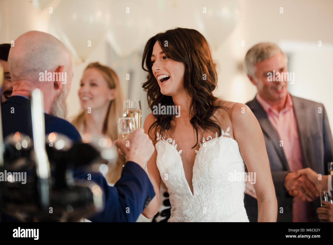 Bella Sposa è socializzare con suo padre e la famiglia il giorno del matrimonio. Essi stanno bevendo champagne e ridere insieme. Foto Stock