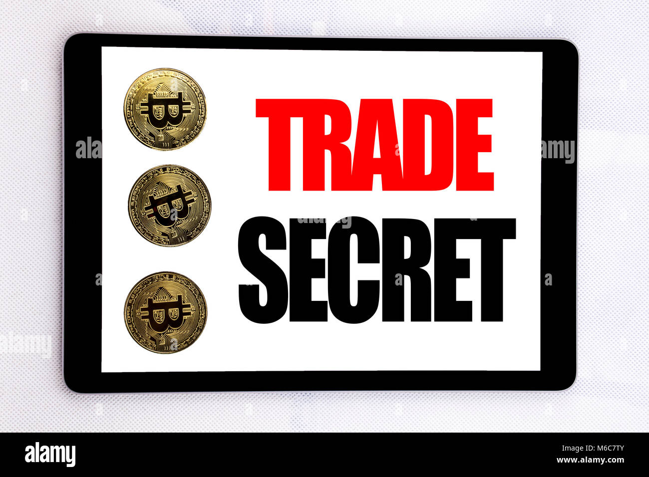 La scrittura di un testo che mostra il segreto commerciale. Il concetto di business per la protezione dei dati scritti su tablet schermo su sfondo bianco con cryptocurrency bitcoin accanto Foto Stock