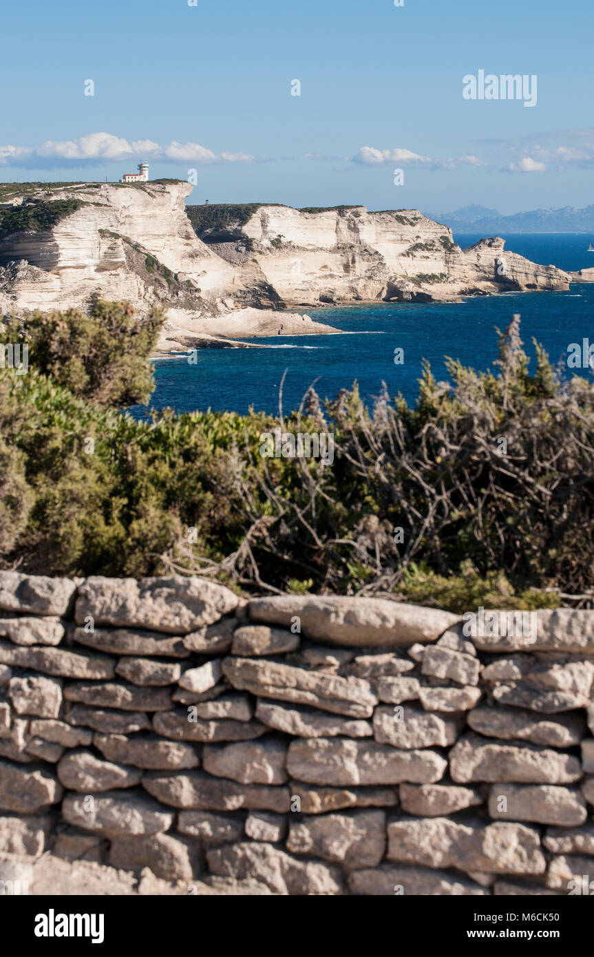 Corsica: muro di pietra e le bianche scogliere calcaree nella International Bouches de Bonifacio parco marino con vista del capo Pertusato faro Foto Stock