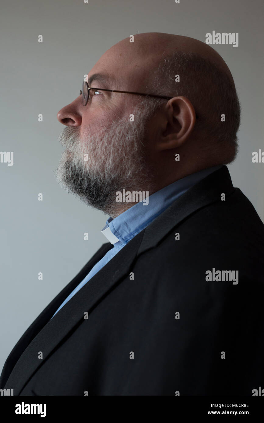 Un vicario maschio con la barba e bicchieri arrotondati guarda lontano dalla telecamera in un ritratto classico pongono Foto Stock