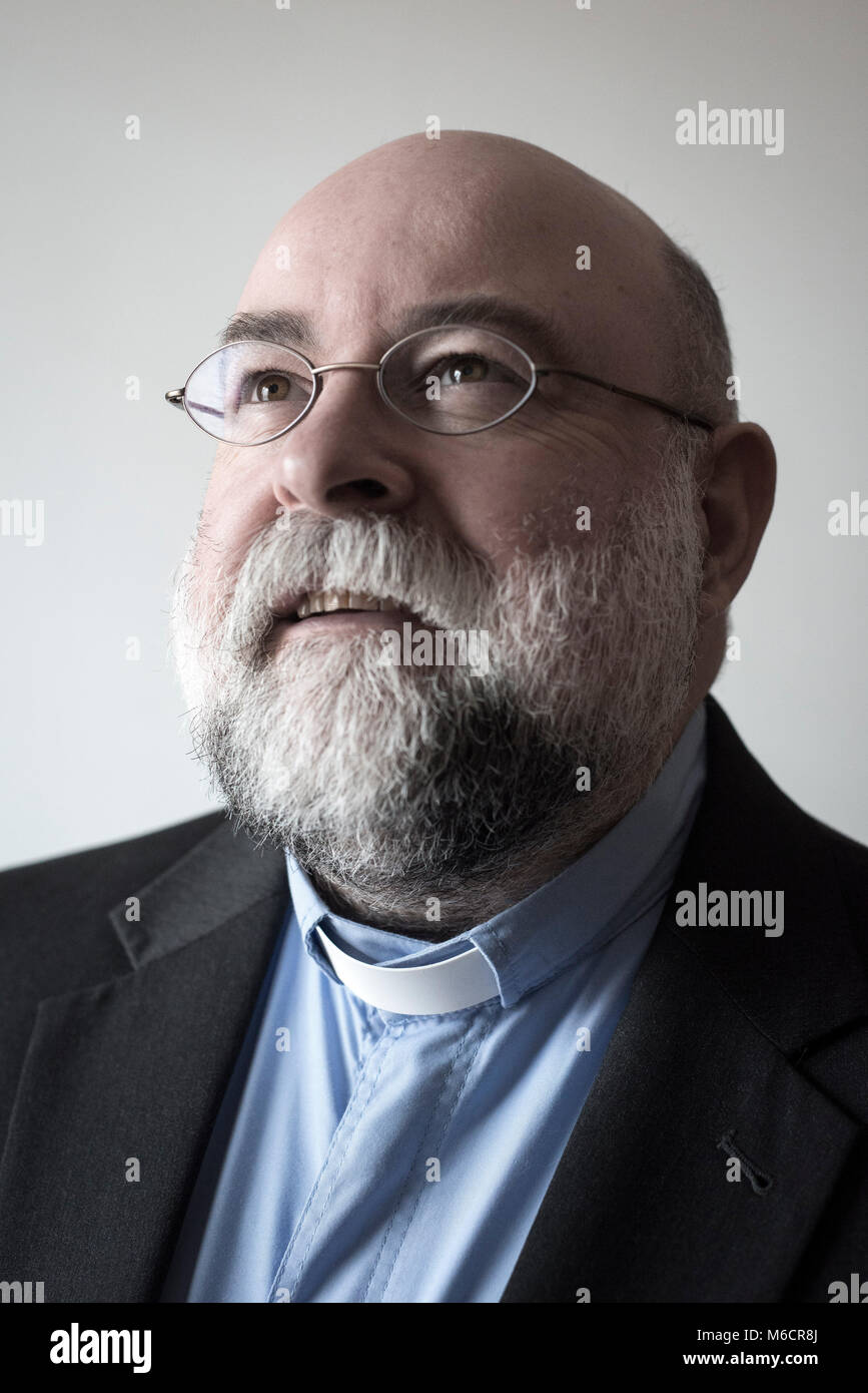 Un vicario maschio con la barba e bicchieri arrotondati guarda lontano dalla telecamera in un ritratto classico pongono Foto Stock