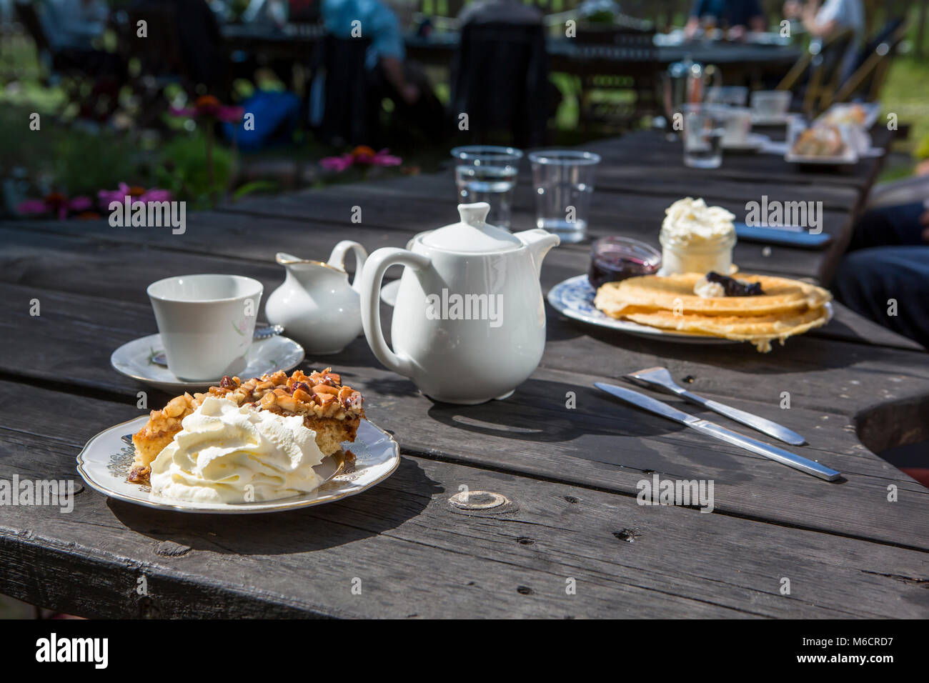 Un tavolo all'aperto con caffè, torte e una lattina di latte. Un tipico fika svedese al sole. Foto Stock
