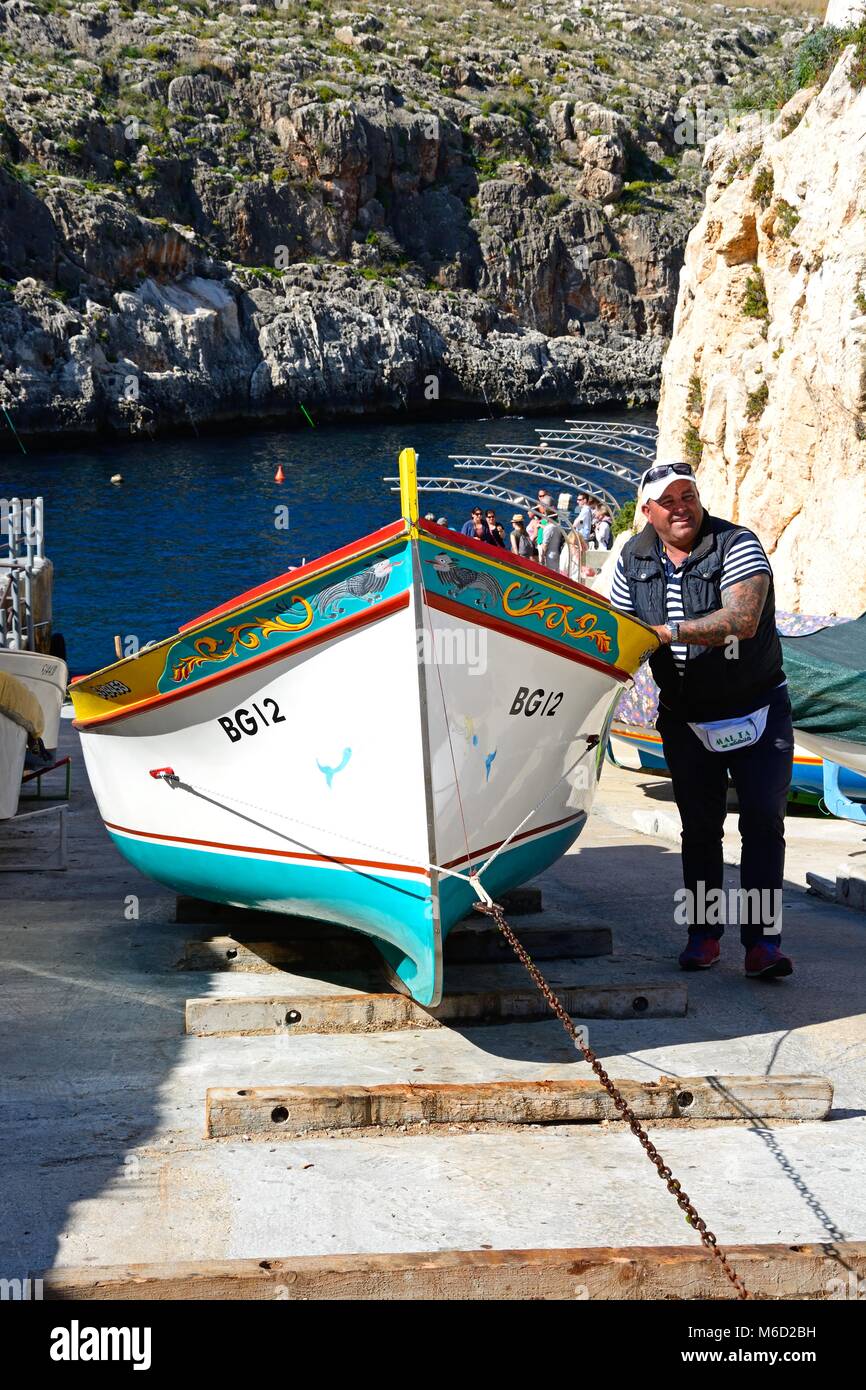 L'uomo tira un Dghajsa tradizionali taxi acqueo fino a rampa per ormeggio al punto di partenza con i turisti in attesa di una barca in fondo, Blue Grotto Foto Stock