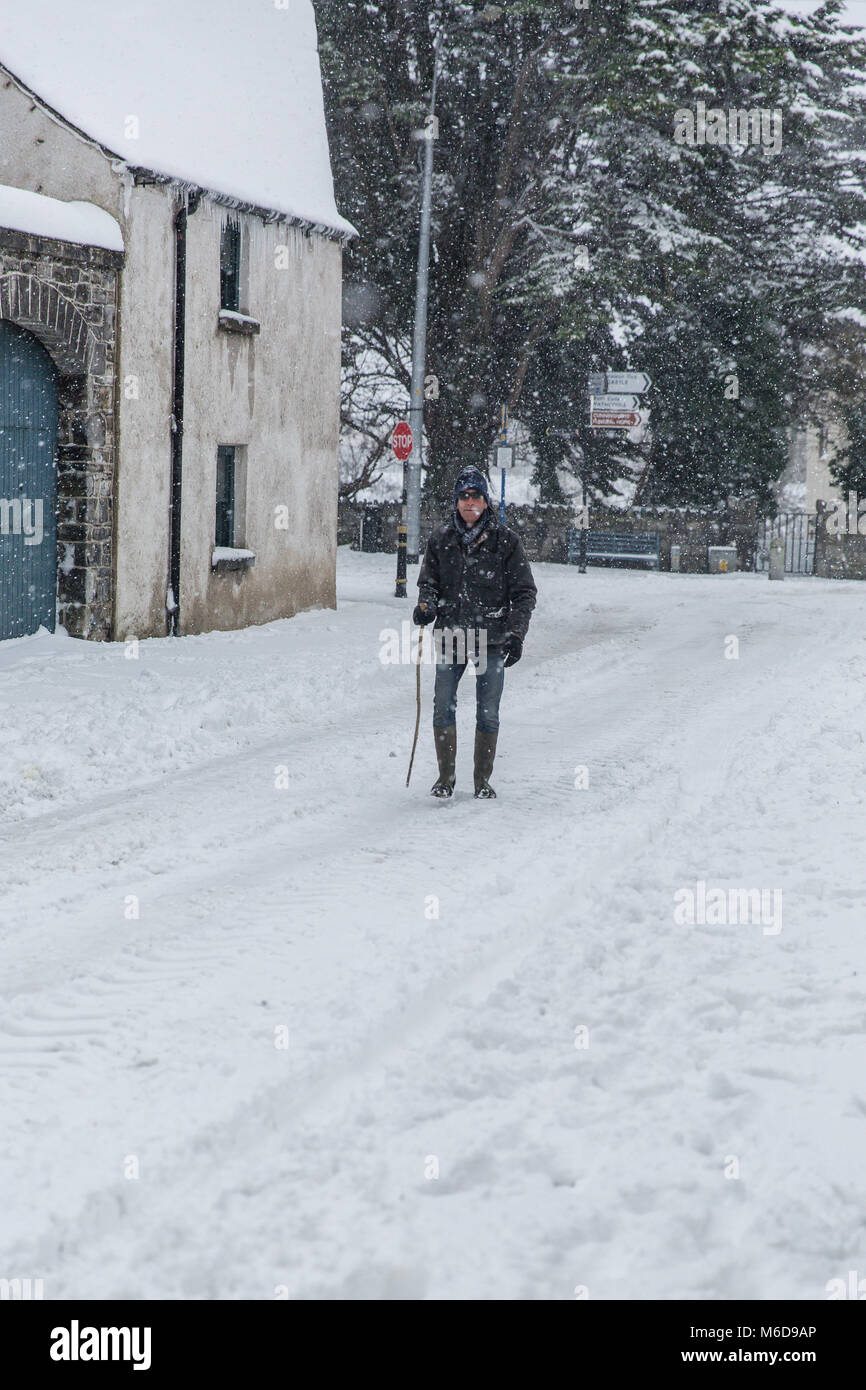 Celbridge, Kildare, Irlanda. 02 MAR 2018: Main Street a Celbridge coperto di neve a seguito dell'ondata di freddo bugged "La Bestia da est' seguita dalla tempesta Emma. Uomo con bastone avente una passeggiata attraverso il centro della coperta di neve road a Celbridge città. Paesaggio invernale. Foto Stock