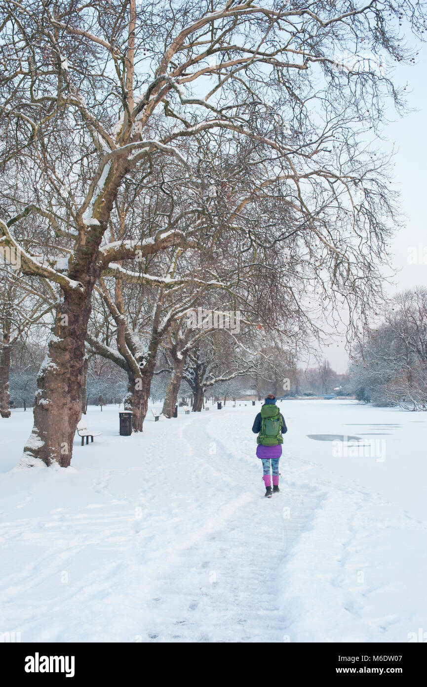 Una donna che cammina lungo una coperta di neve nel percorso di Regents Park durante la stagione invernale,(la mattina presto, febbraio 2018), London, Regno Unito Foto Stock