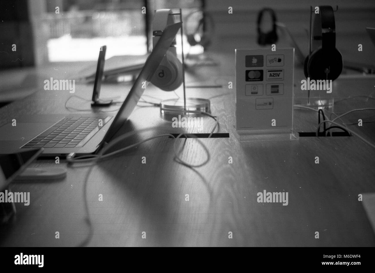 I macbook, smartphone e hearphones su una scrivania di legno con Apple paga e carta di credito banner. Apple Store in Piazza della Repubblica, Firenze Italia Foto Stock
