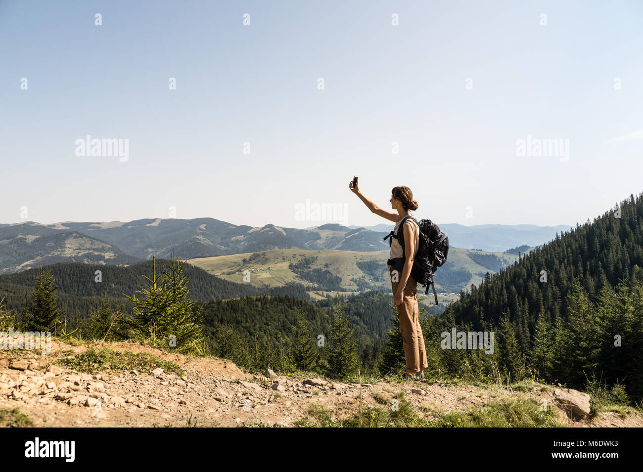 Ragazza con zaino turistico su una lunga escursione a piedi alla ricerca di telefono cellulare la connessione di rete su in collina Foto Stock