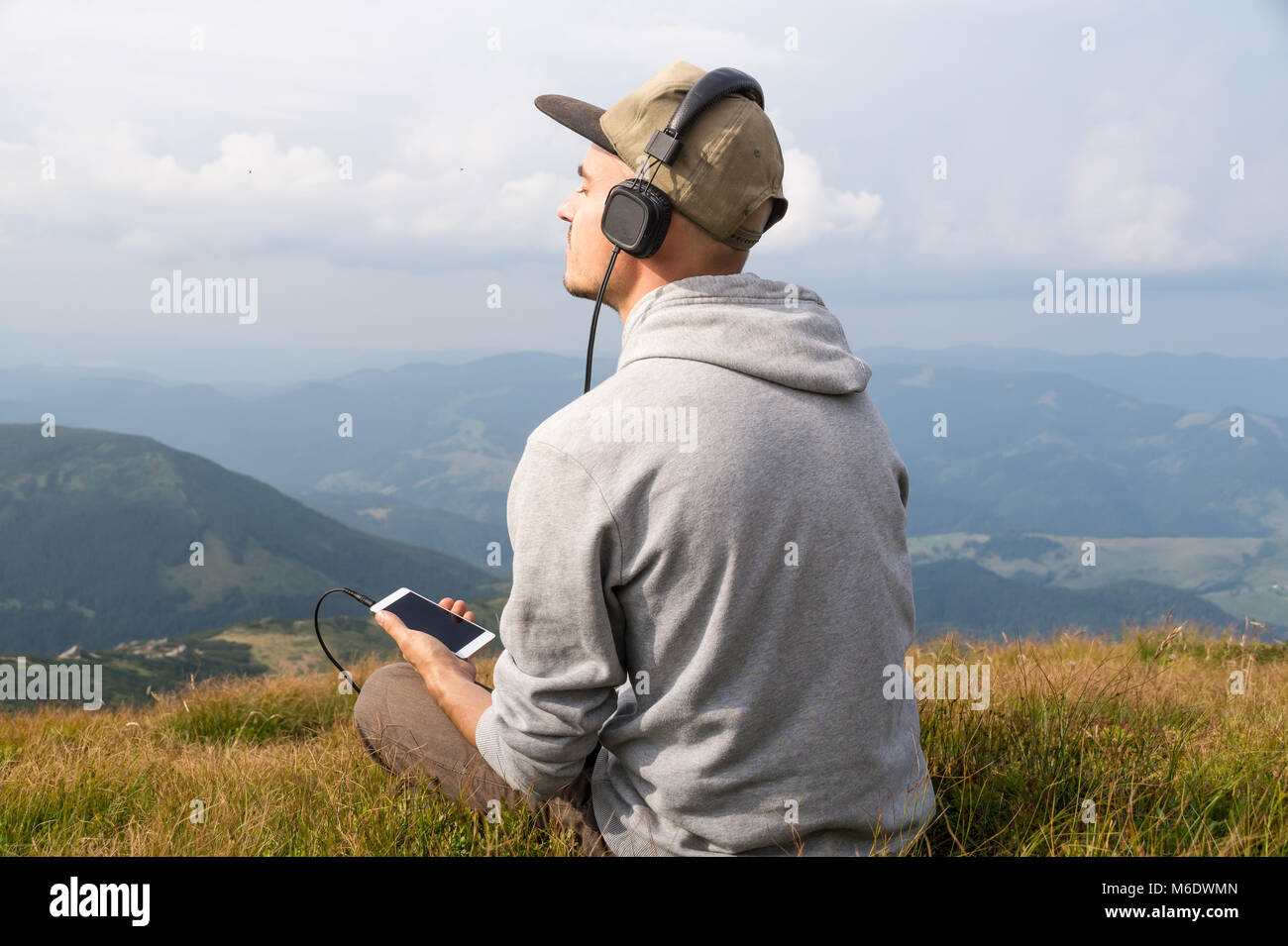 Uomo si siede in cima alla collina nei Carpazi e ascolta la musica in cuffia e gode di uno splendido scenario Foto Stock