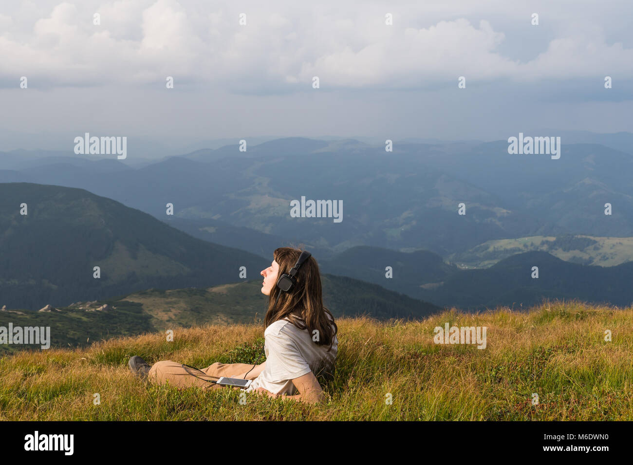Escursionista femmina in cuffia con un telefono cellulare su un prato di montagna Foto Stock