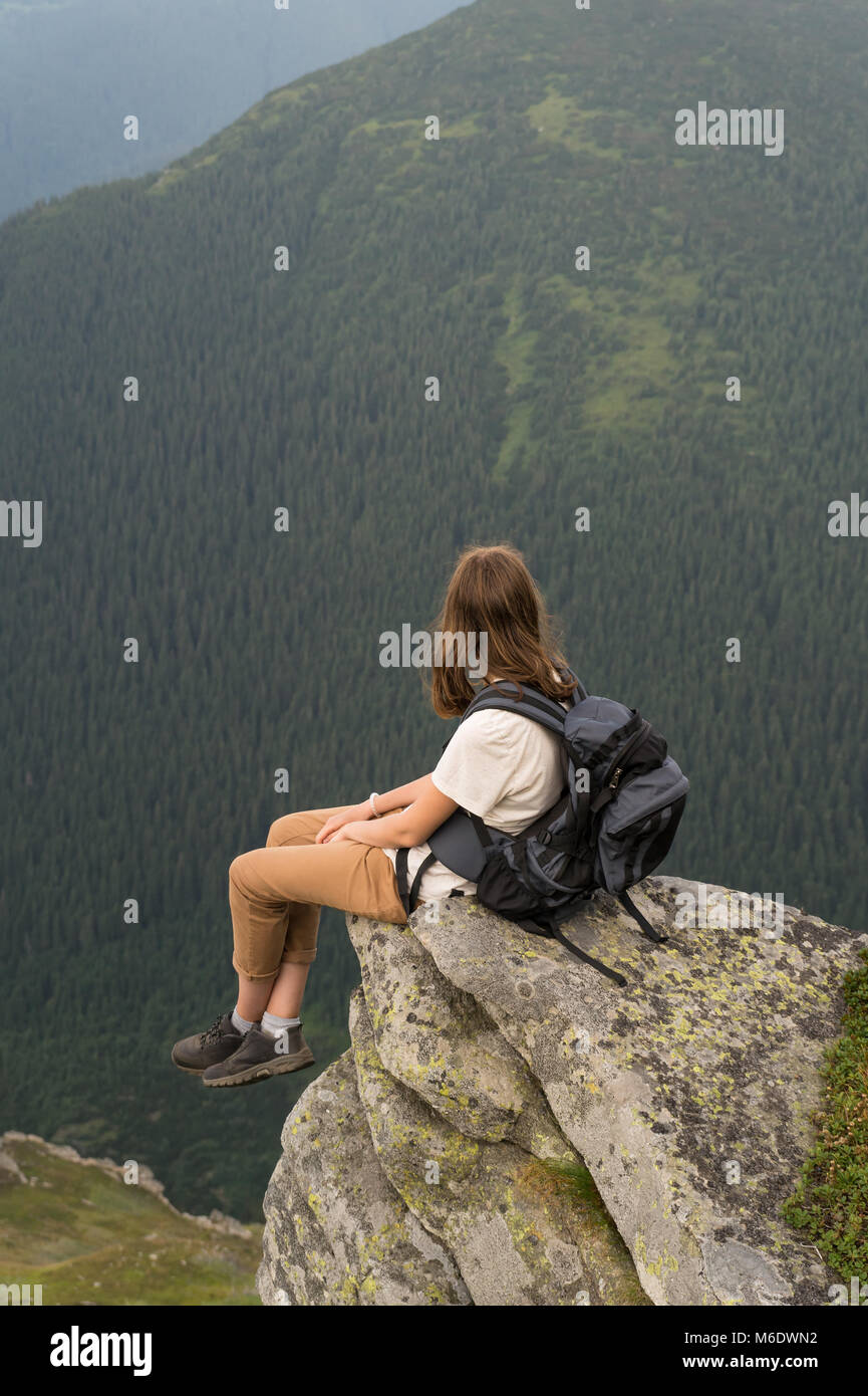 Turista femminile si siede sulla roccia in zona di montagna e rilassa dopo aver camminato fino a destinazione Foto Stock