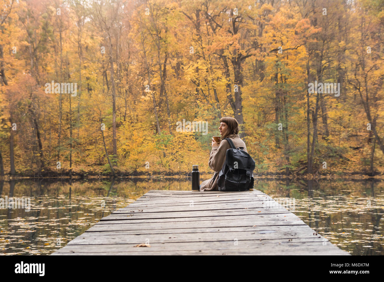 Giovani femmine escursionista con zaino si siede a riverbank, beve caffè e guarda al bellissimo Indian scenario estivo Foto Stock