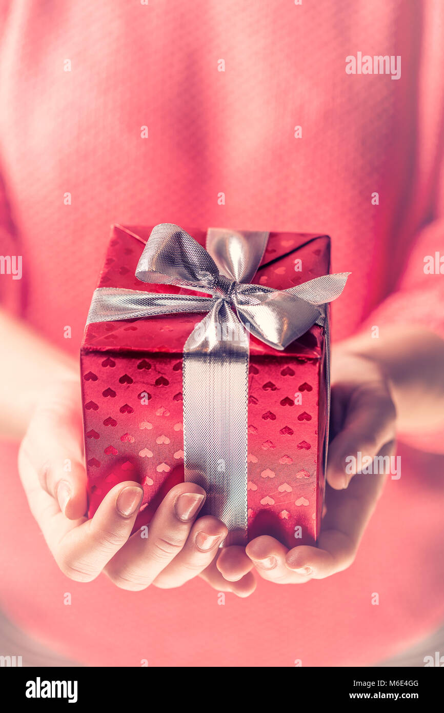 Mani femminili tenendo un regalo rossa avvolto con nastro argentato. Dono di nozze di san valentino compleanno womens giorno o festa della mamma. Foto Stock