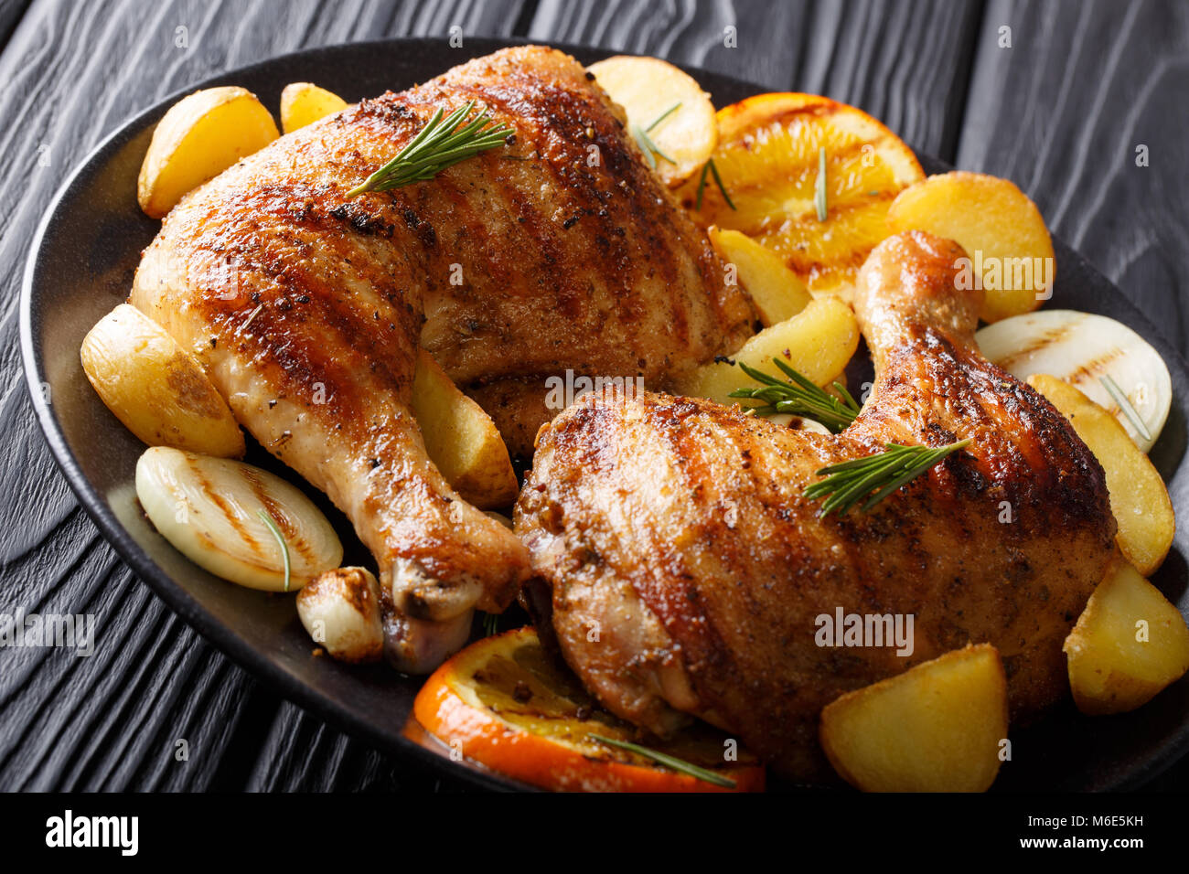 Barbecue in casa: Grigliate le cosce di pollo con arancia, limone, cipolle, aglio e patate Close-up su una piastra sul tavolo orizzontale. Foto Stock