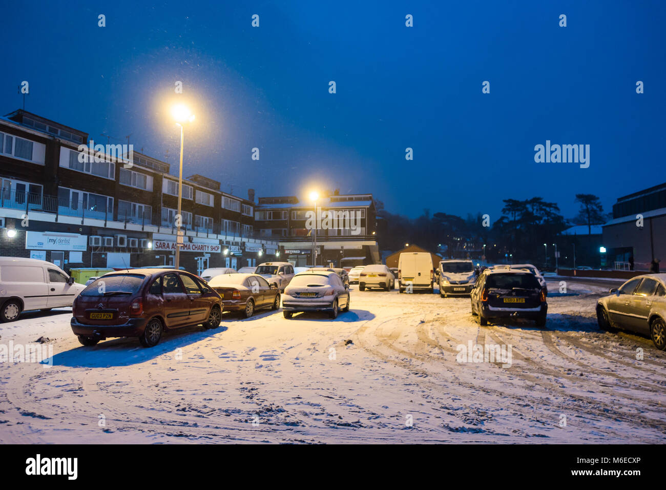 Auto parcheggiata in un parcheggio che è coperto di neve a notte. Foto Stock