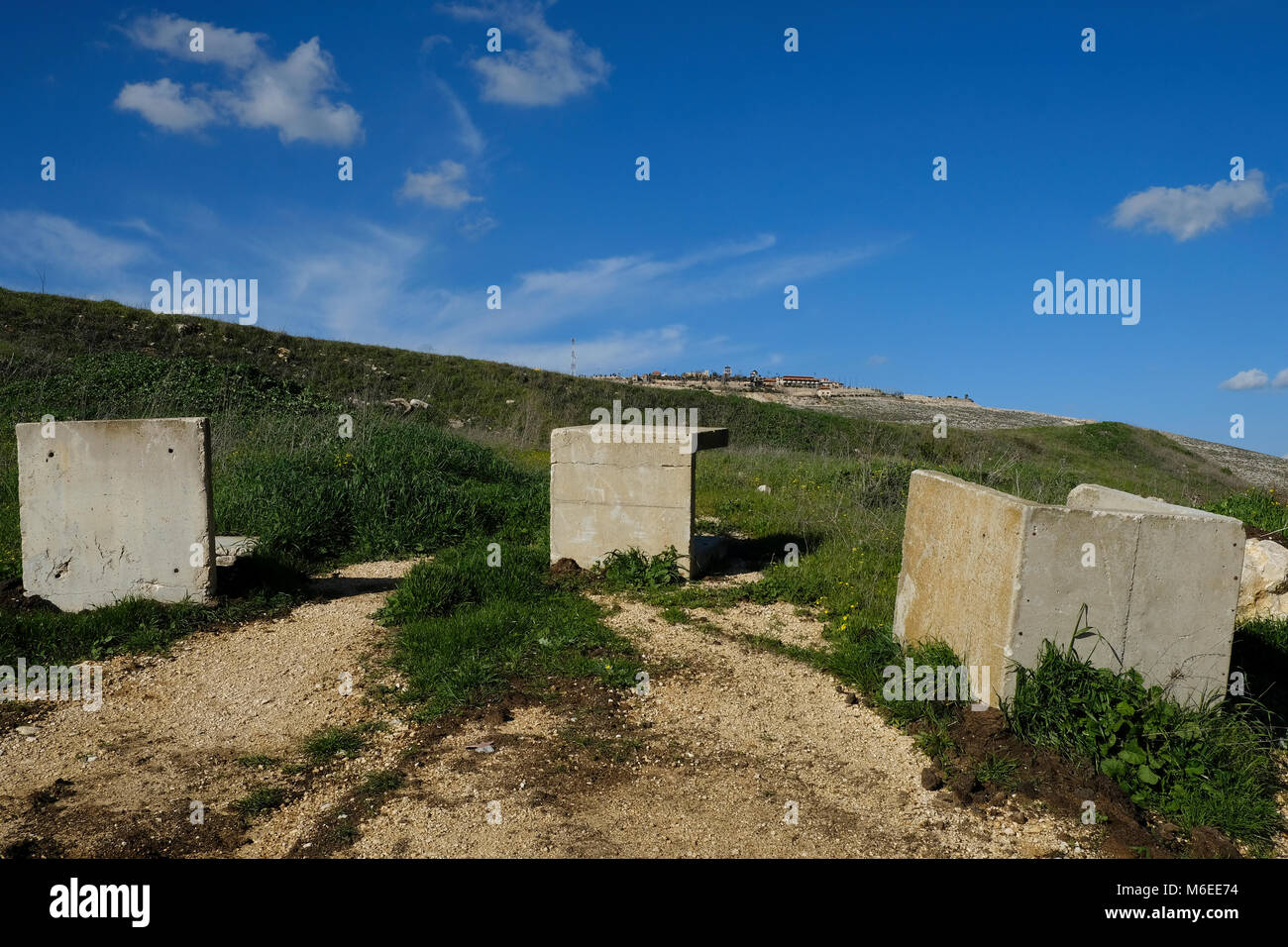 Vista del calcestruzzo barricate dell'esercito israeliano con vista in lontananza il villaggio libanese di Maroun al-Ras, accoccolato in Jabal Amel (Monte Amel) nel nord di Israele Foto Stock