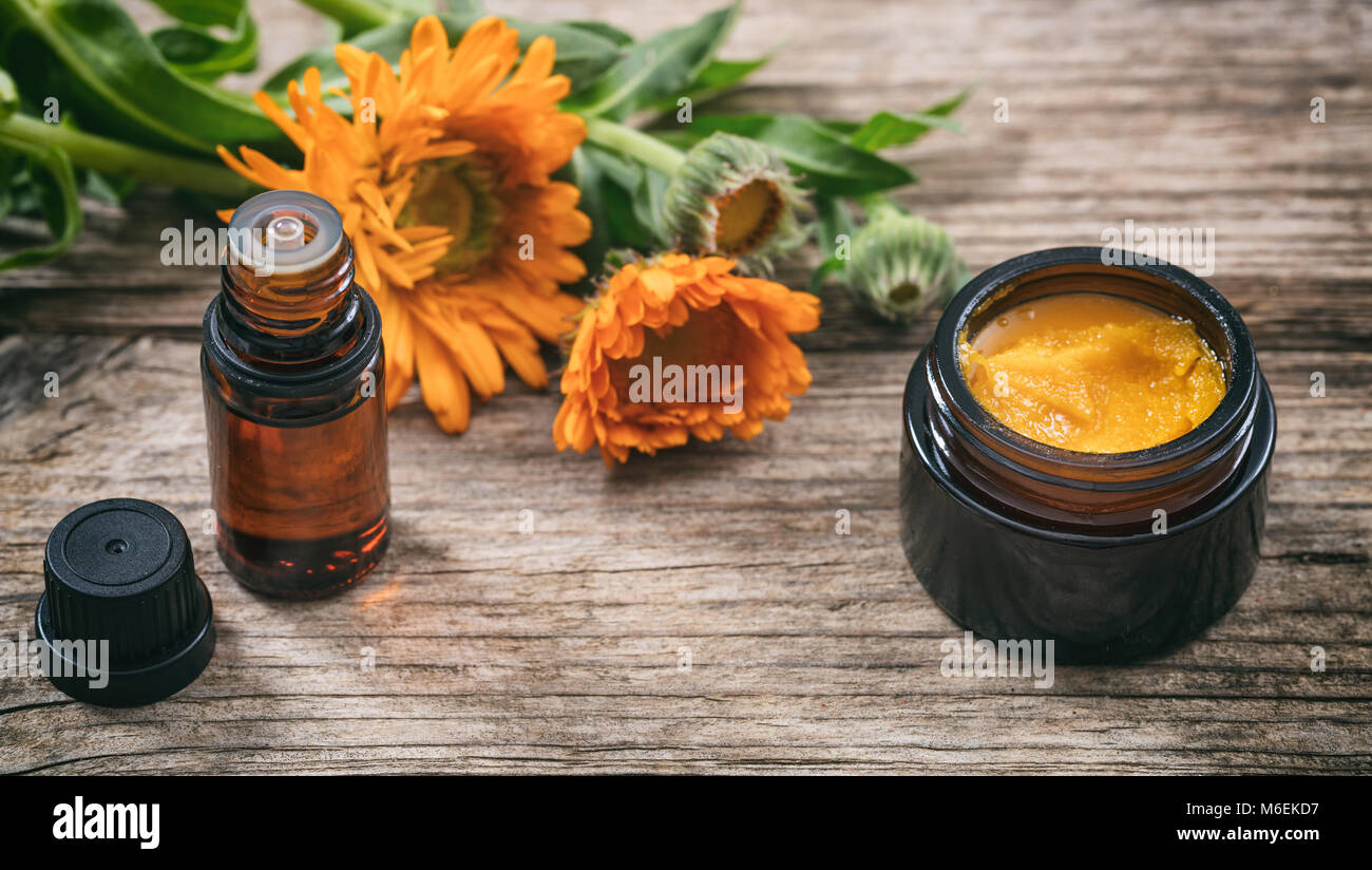 Calendula prodotti. Olio essenziale e un unguento su una tavola di legno, fresche blooming calendula sfondo, Foto Stock
