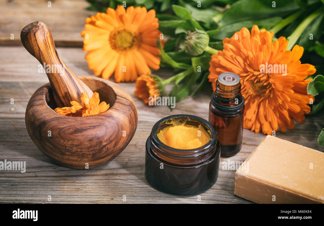 Calendula prodotti. Olio essenziale, unguento e un mortaio su una tavola di legno, fresche blooming calendula sfondo, Foto Stock