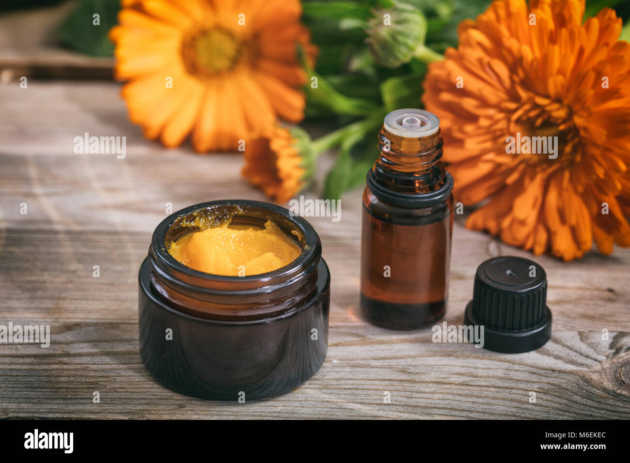 Calendula prodotti. Olio essenziale e un unguento su una tavola di legno, fresche blooming calendula sfondo, Foto Stock