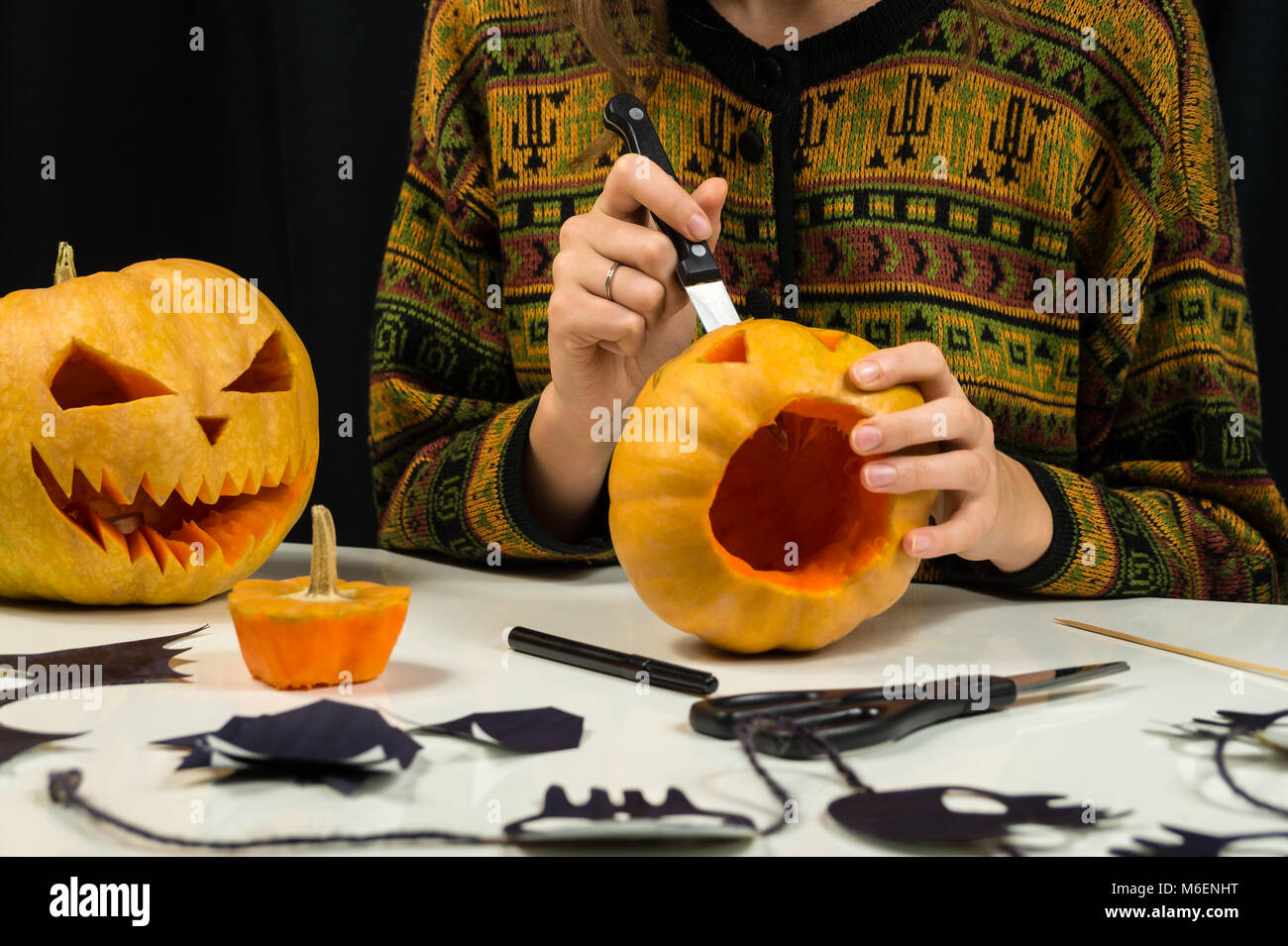 Persona di sesso femminile si prepara la decorazione per la festa di Halloween e rende scary pumpkin volti a un tavolino da soggiorno Foto Stock