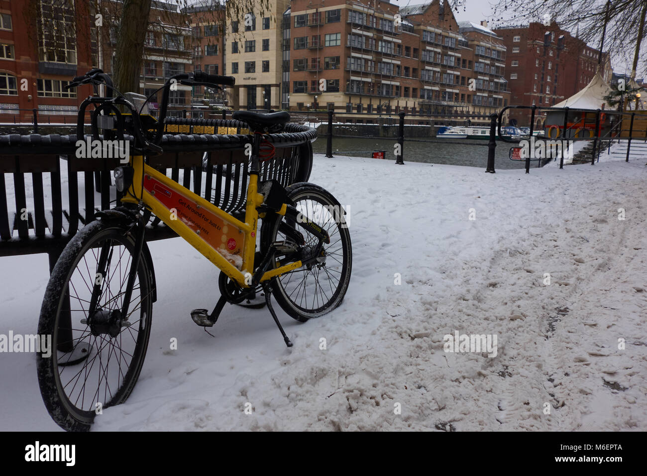 Il noleggio di una bicicletta da Bristol YoBike del regime britannico in appoggio contro un banco a cannoni Marsh, nella neve dalla tempesta Emma Foto Stock