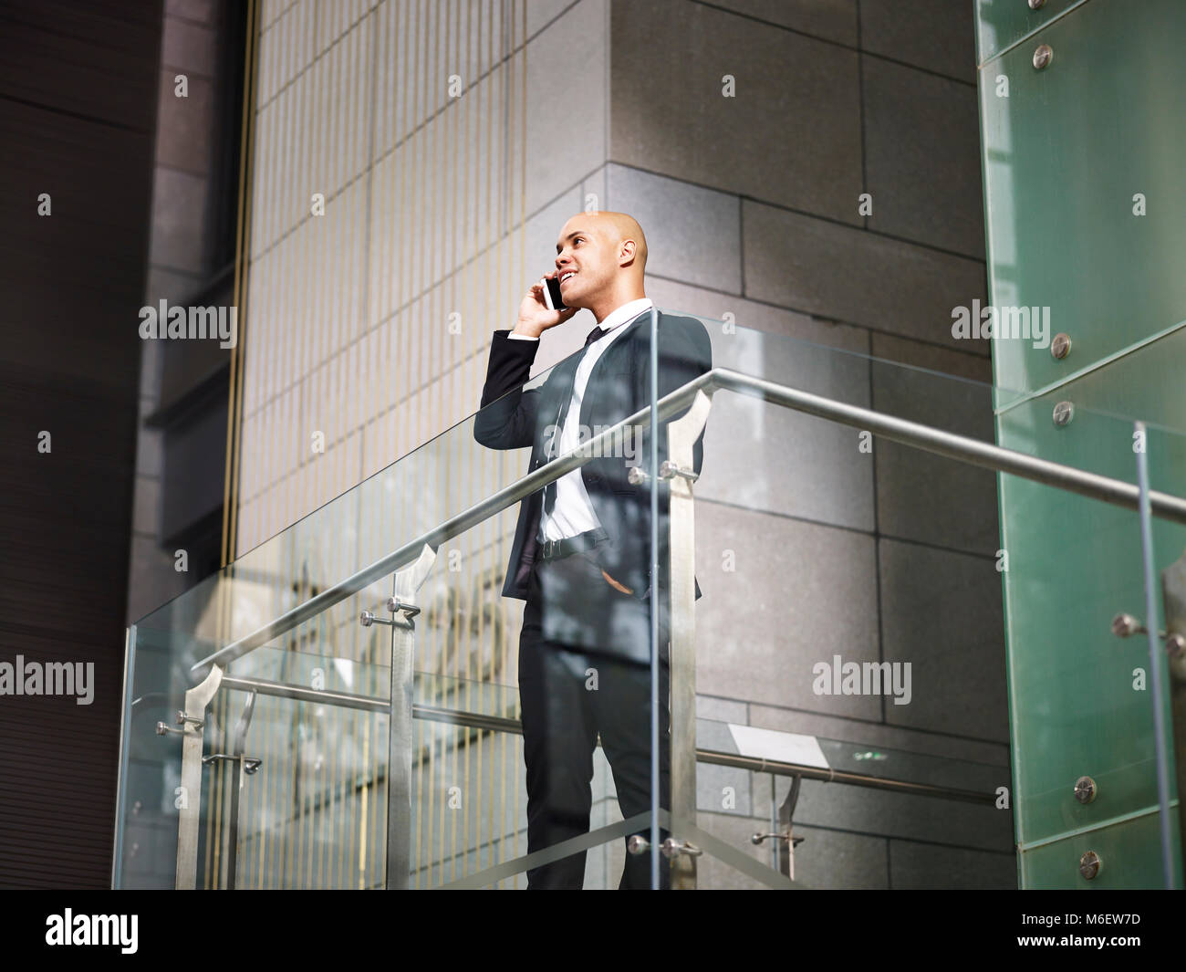 Latin American corporate executive business man in piedi in cima alle scale come effettuare una chiamata utilizzando il telefono cellulare in un ufficio moderno edificio, basso angolo di visione. Foto Stock