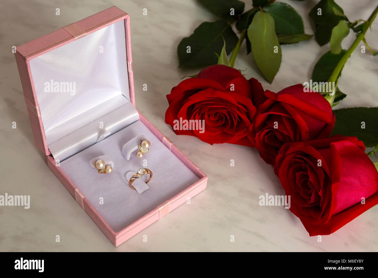 Orecchini perla e golden ring in una confezione regalo con rose rosse su sfondo marmo. Nozze, il giorno di san valentino Foto Stock