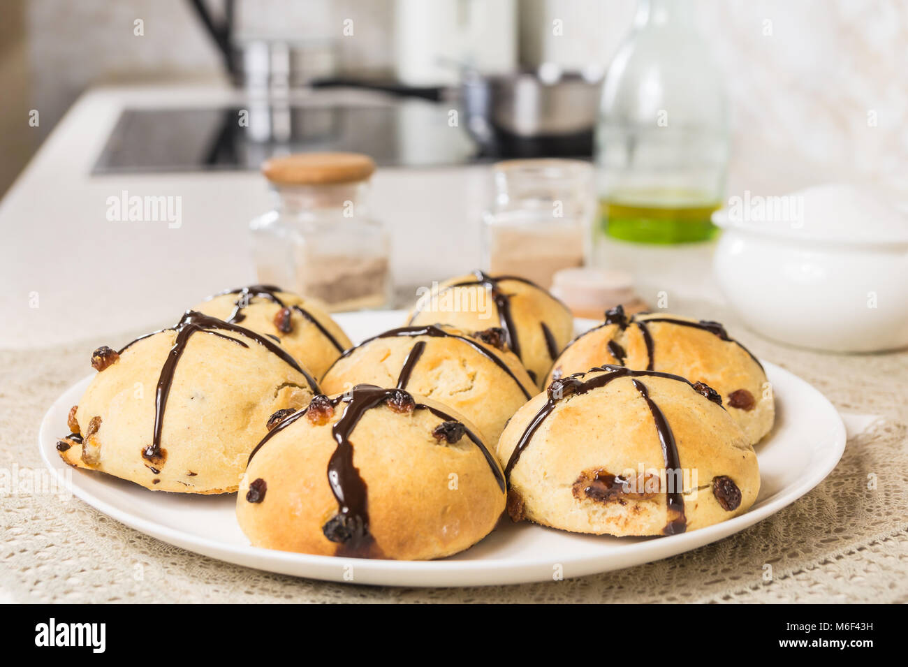 Close-up di immagine sfornati freschi panini a croce. Fatta in Casa dolce di Pasqua il pane sulla tavola servita su piastra bianca nel moderno ambiente cucina Foto Stock