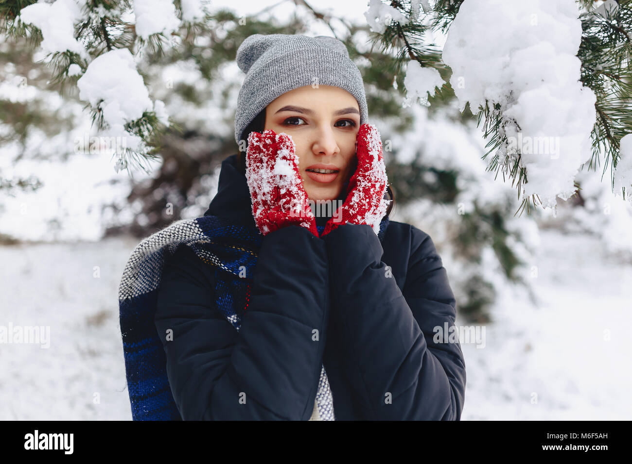 La ragazza warmes suo guance in guanti con il freddo inverno nella foresta di pini coperti di neve Foto Stock