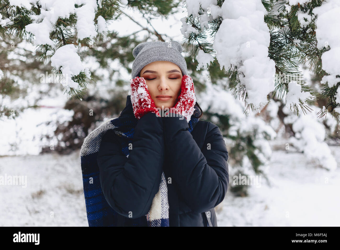 La ragazza warmes suo guance in guanti con il freddo inverno nella foresta di pini coperti di neve Foto Stock