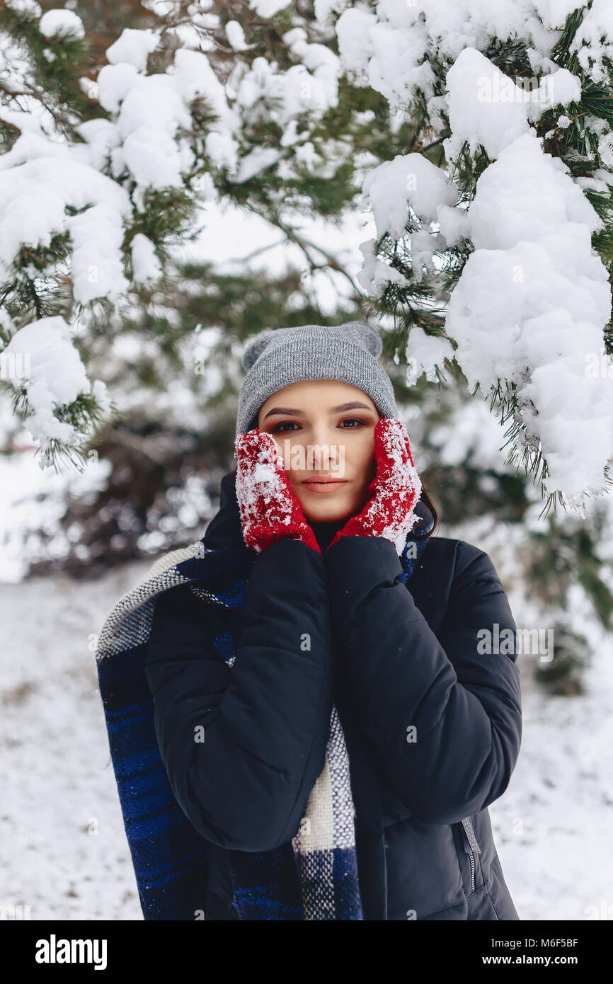 La ragazza warmes suo guance in guanti con il freddo inverno nella foresta di pini coperti di neve Foto Stock