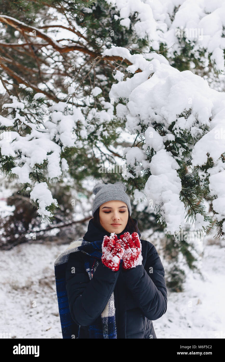 La ragazza warmes suo guance in guanti con il freddo inverno nella foresta di pini coperti di neve Foto Stock