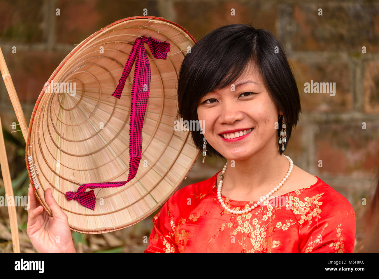 Una bella donna vietnamita che indossa un abito rosso e un bambù cappello conico ad Hanoi, Vietnam Foto Stock