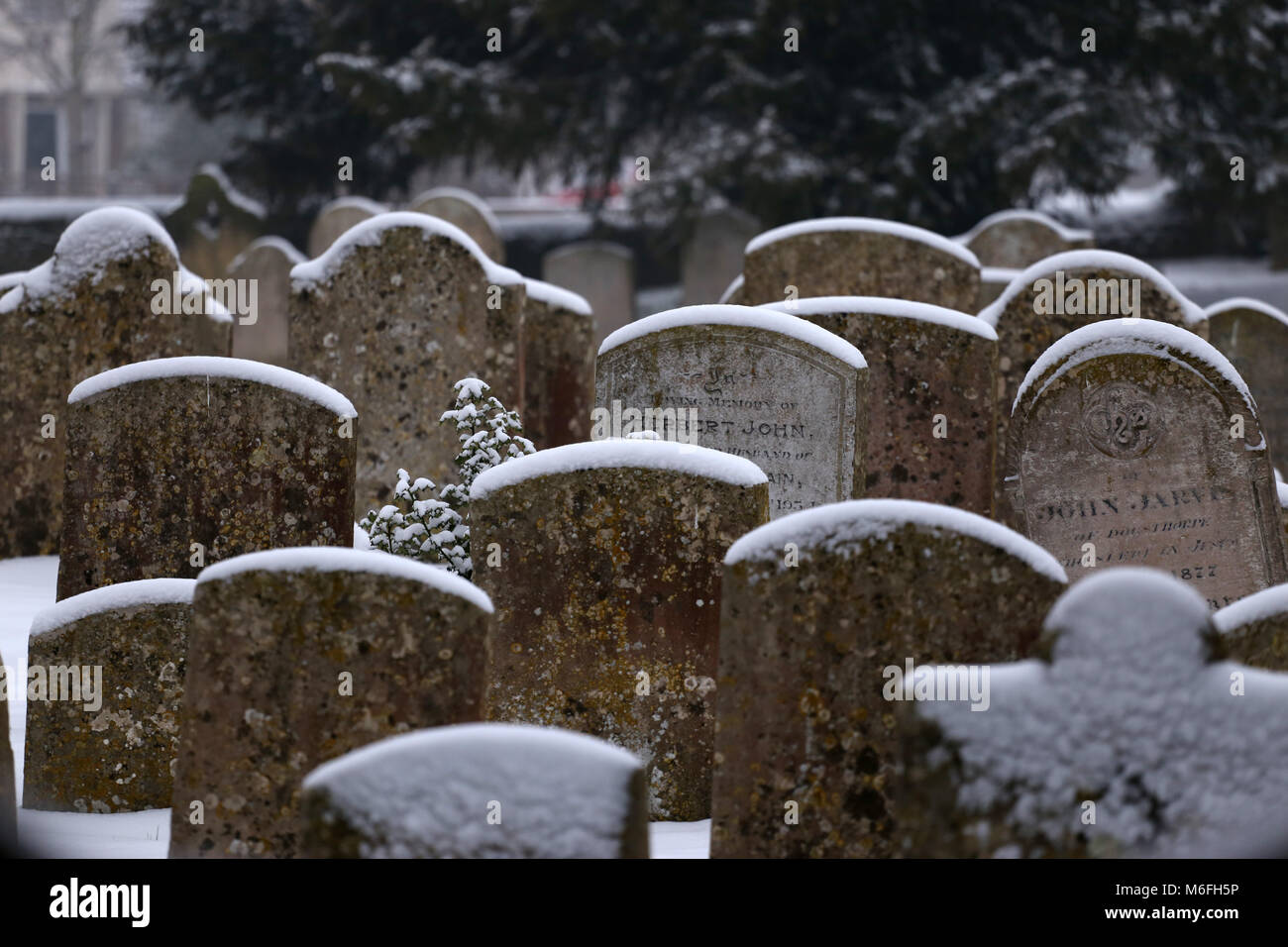 Grave lapidi nella coperta di neve Chiesa di Tutti i Santi sagrato, in Peterborough, CAMBRIDGESHIRE. Neve, Peterborough, il 3 marzo 2018. Foto Stock