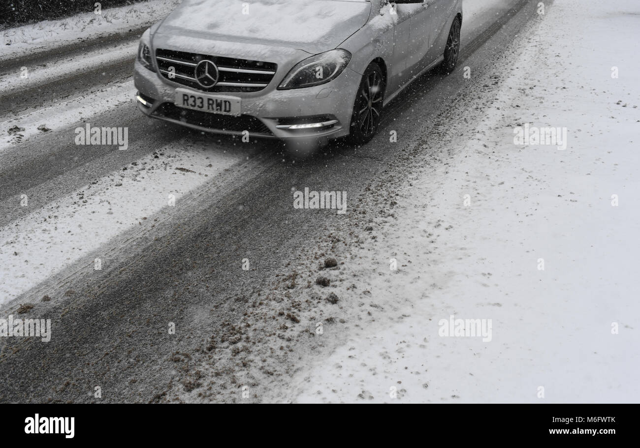Una chiusura delle ruote e il cofano del motore di un argento mercedes guida auto in strada coperta di neve sulla A36. Foto Stock