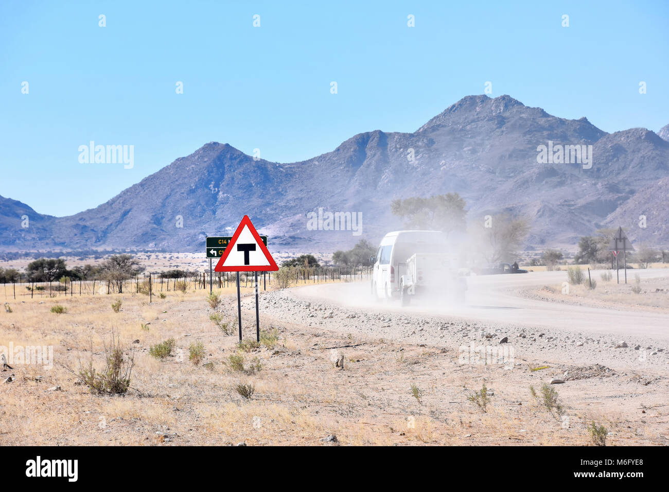 Una giunzione a t un cartello stradale vicino alla città di solitario in Namibia in Sud Africa con un veicolo passando da su una strada di ghiaia in polvere contro la montagna Foto Stock