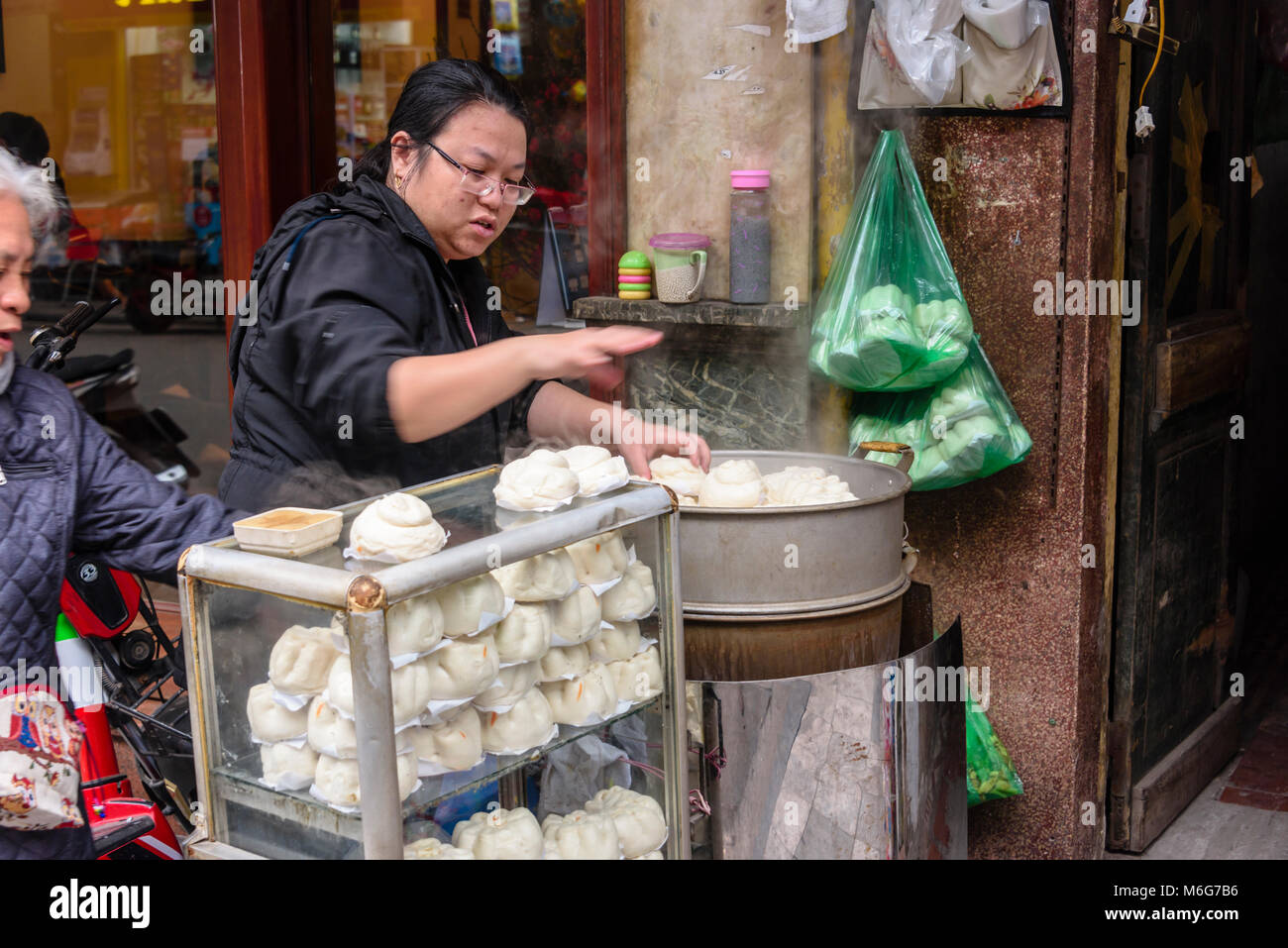 Una donna cuochi bao bun, un pane cotto a vapore street food snack sul sentiero di Hanoi, Vietnam Foto Stock