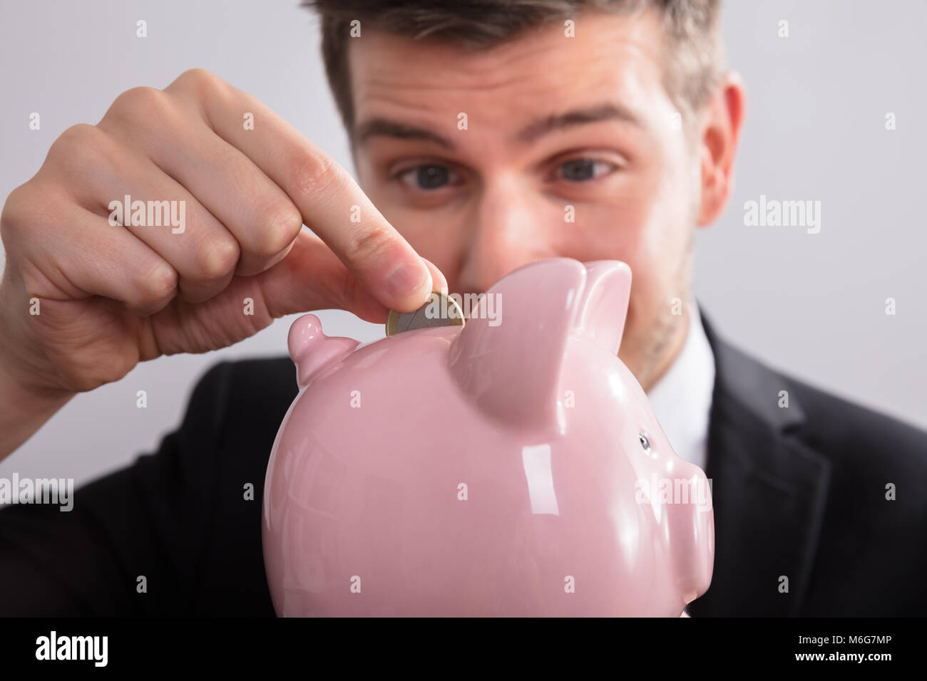 Close-up di un imprenditore inserimento di moneta in rosa Piggybank Foto Stock