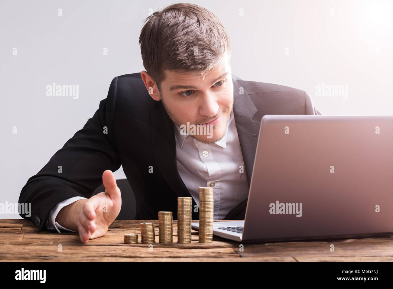 Imprenditore lavorando sul computer portatile con monete impilate sulla scrivania in legno Foto Stock