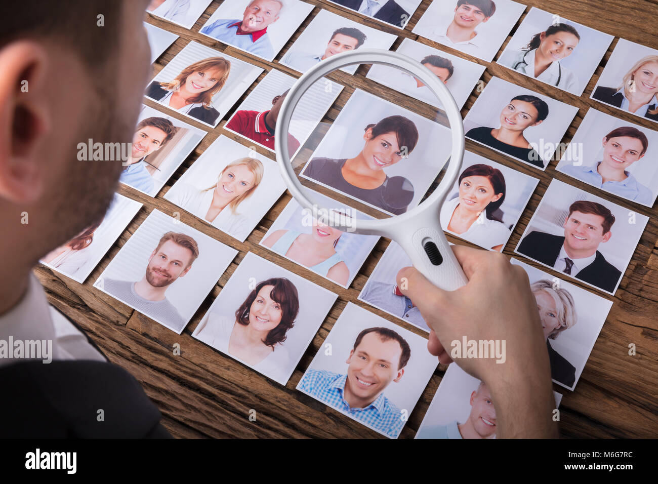 Close-up di un imprenditore la mano guardando al candidato la fotografia con lente di ingrandimento sulla scrivania Foto Stock