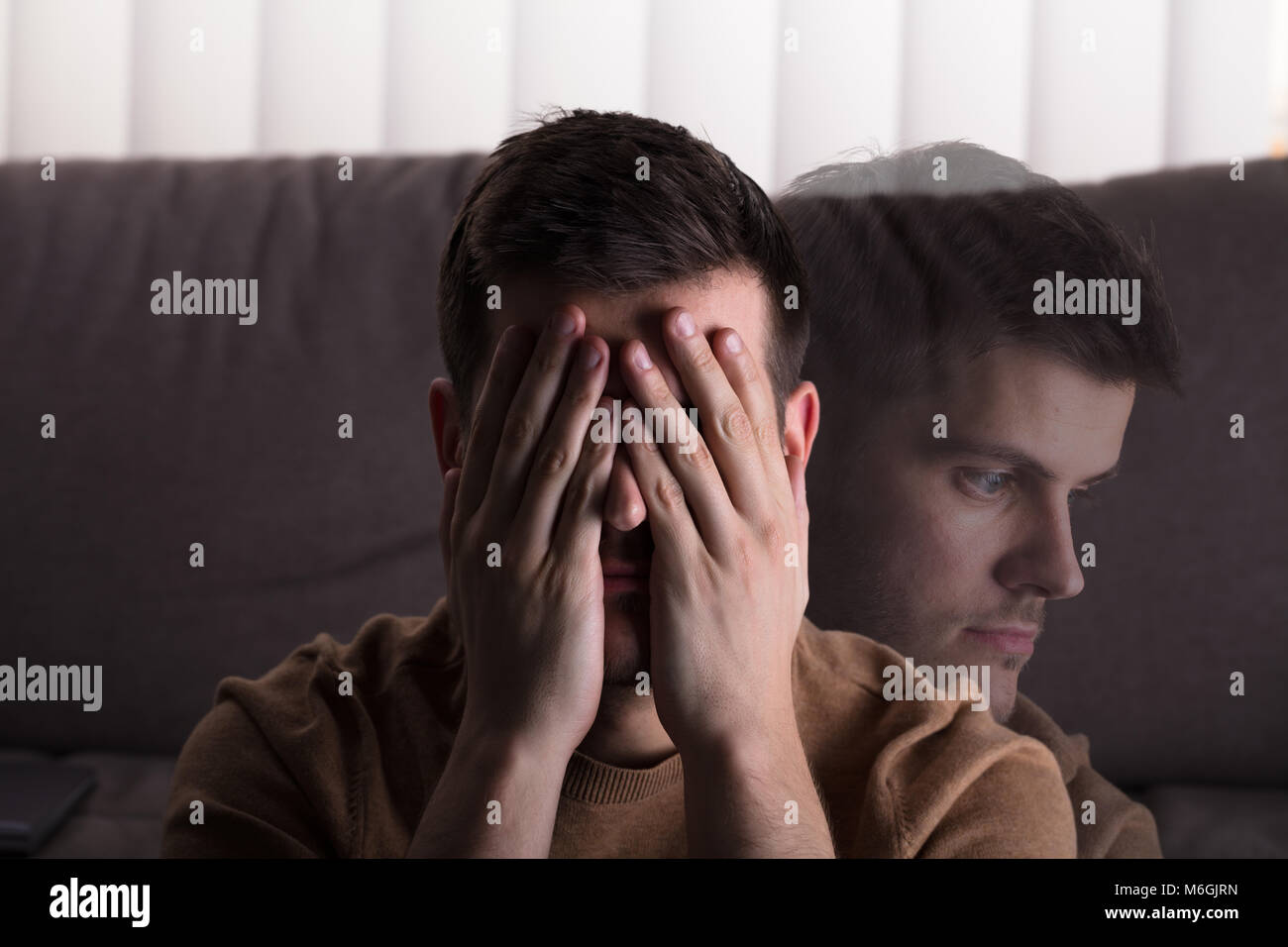 Giovane triste uomo seduto nella parte anteriore del divano di casa Foto Stock