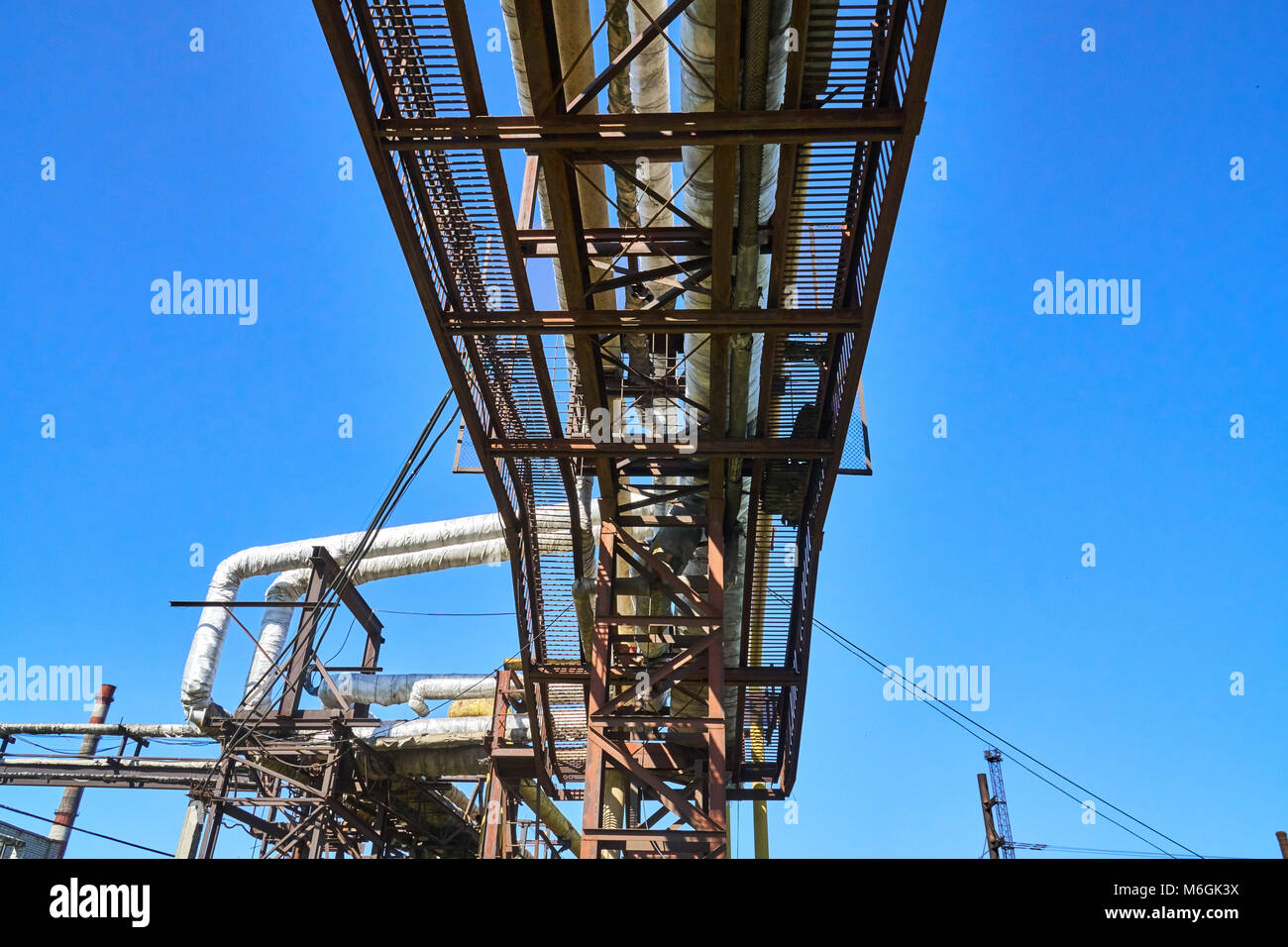Collegare la conduttura al di sopra del condotto di riscaldamento a terra dell'impianto metallurgico contro il cielo blu Foto Stock
