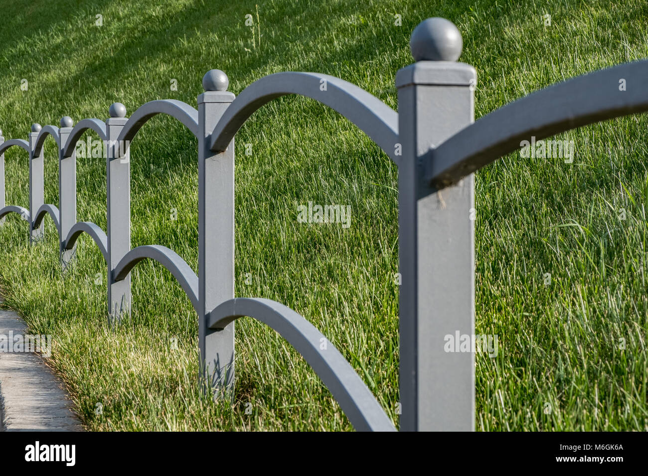 Sofisticata recinzione in metallo grigio con erba verde sullo sfondo, barre curve e cappucci sferici per pali creano una barriera esteticamente piacevole Foto Stock