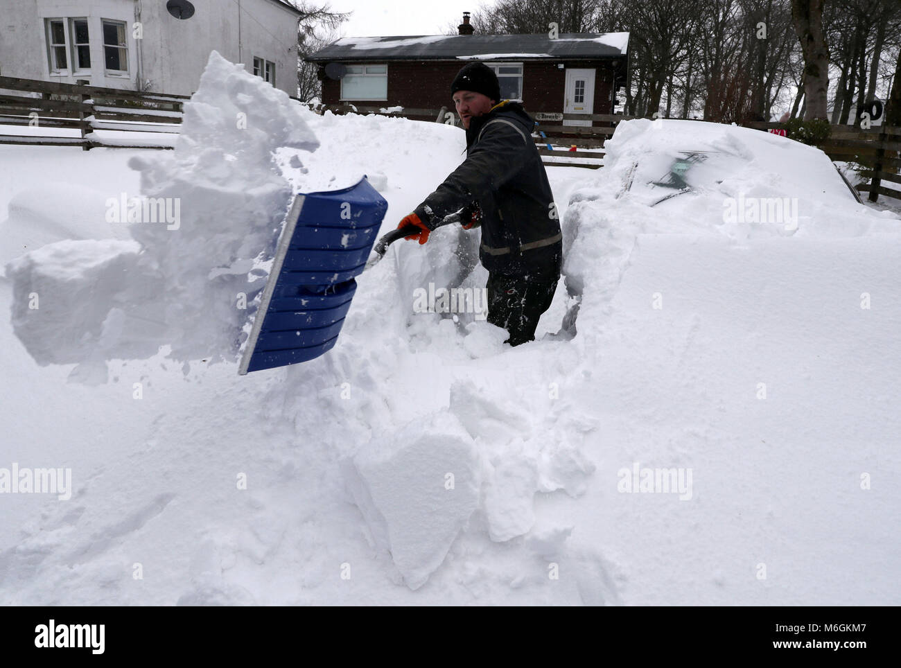 Peter Laidlaw tenta di cancellare la neve e la deriva che ha sommerso i propri veicoli a casa sua in rurale Carron Valley vicino a Stirling durante il recente clima freddo. Foto Stock
