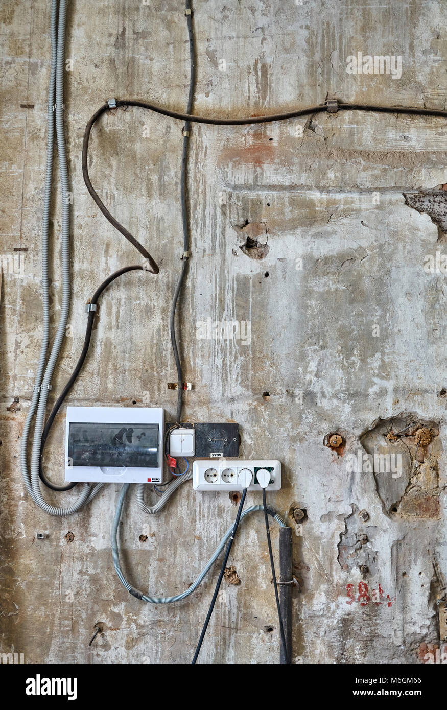 Vecchia parete di cemento che si stacca ricoperta di accessori per cablaggi, quadro di distribuzione elettrica e prese elettriche in un'officina Foto Stock