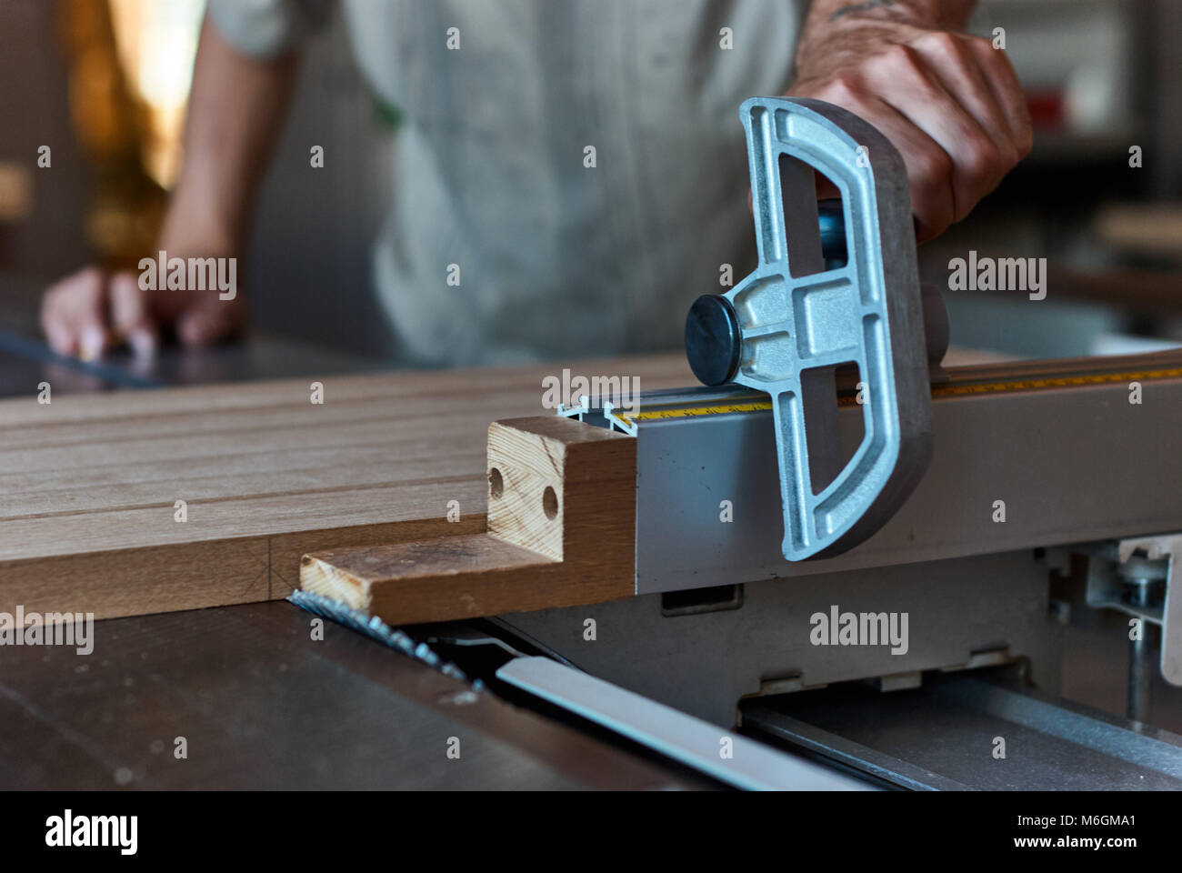 Carpentiere non riconoscibile che utilizza una sega da tavolo affilata per tagliare il pannello in legno incollato durante il lavoro in officina professionale Foto Stock