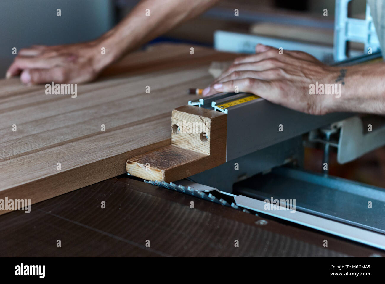 Carpentiere non riconoscibile che utilizza una sega da tavolo affilata per tagliare il pannello in legno incollato durante il lavoro in officina professionale Foto Stock