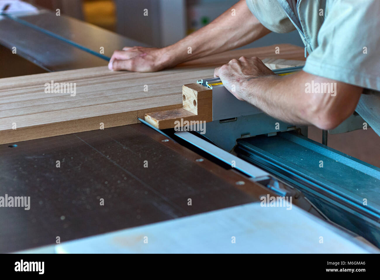 Carpentiere non riconoscibile che utilizza una sega da tavolo affilata per tagliare il pannello in legno incollato durante il lavoro in officina professionale Foto Stock