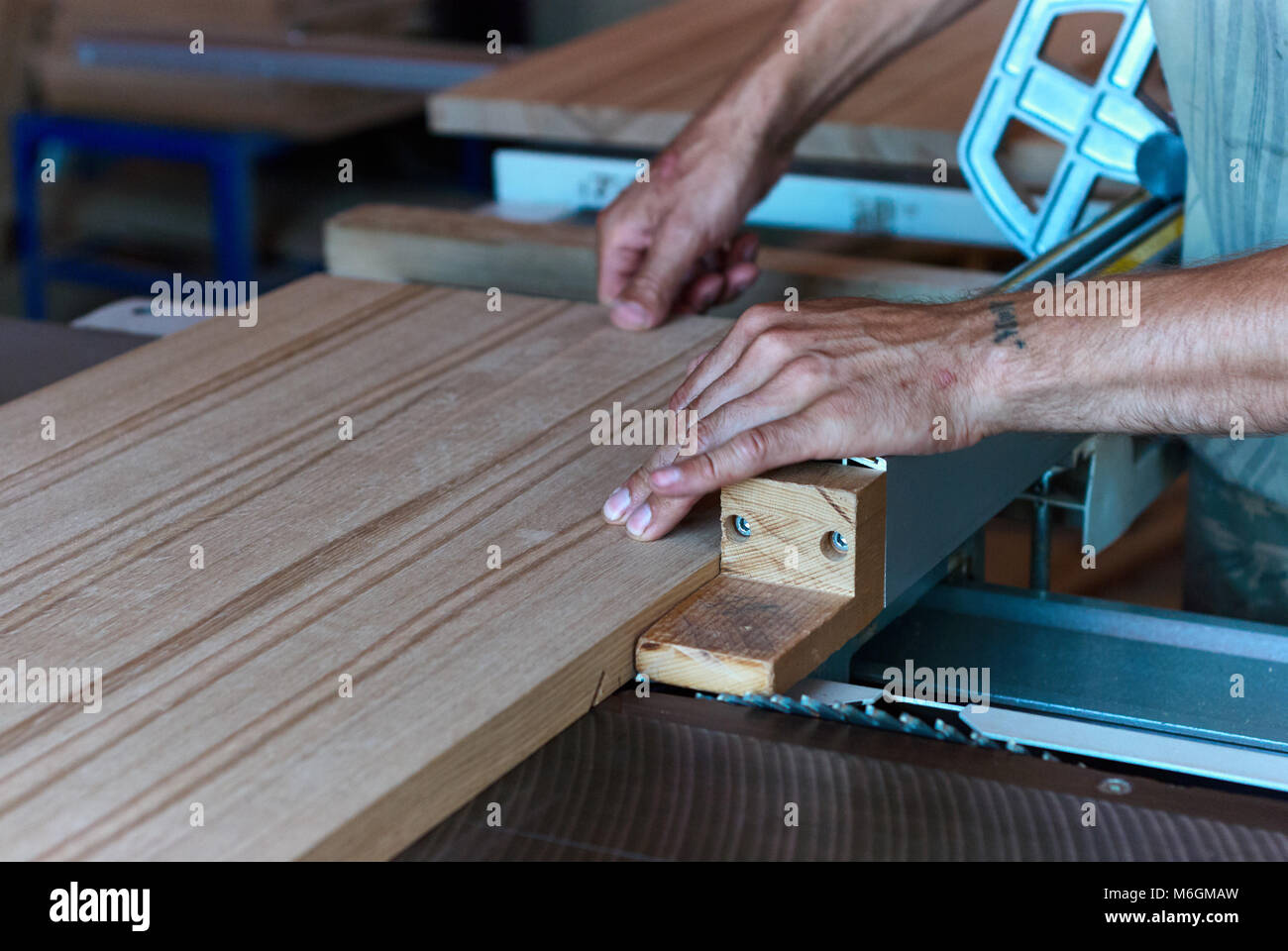 Carpentiere non riconoscibile che utilizza una sega da tavolo affilata per tagliare il pannello in legno incollato durante il lavoro in officina professionale Foto Stock